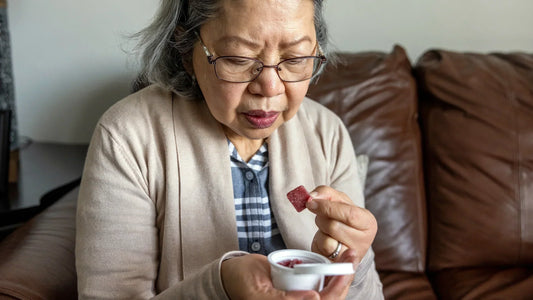 Senior woman holding a gummy supplement, representing calm and wellness.