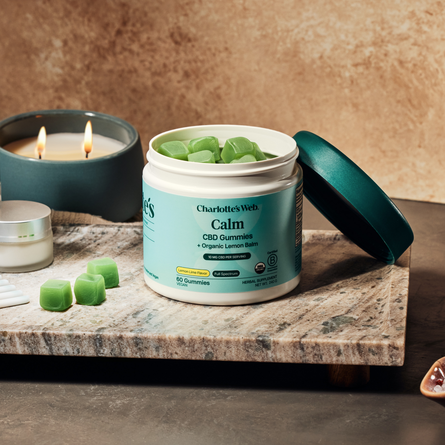 Open jar of Charlotte's Web Calm CBD Gummies on a marble surface with candles in the background.