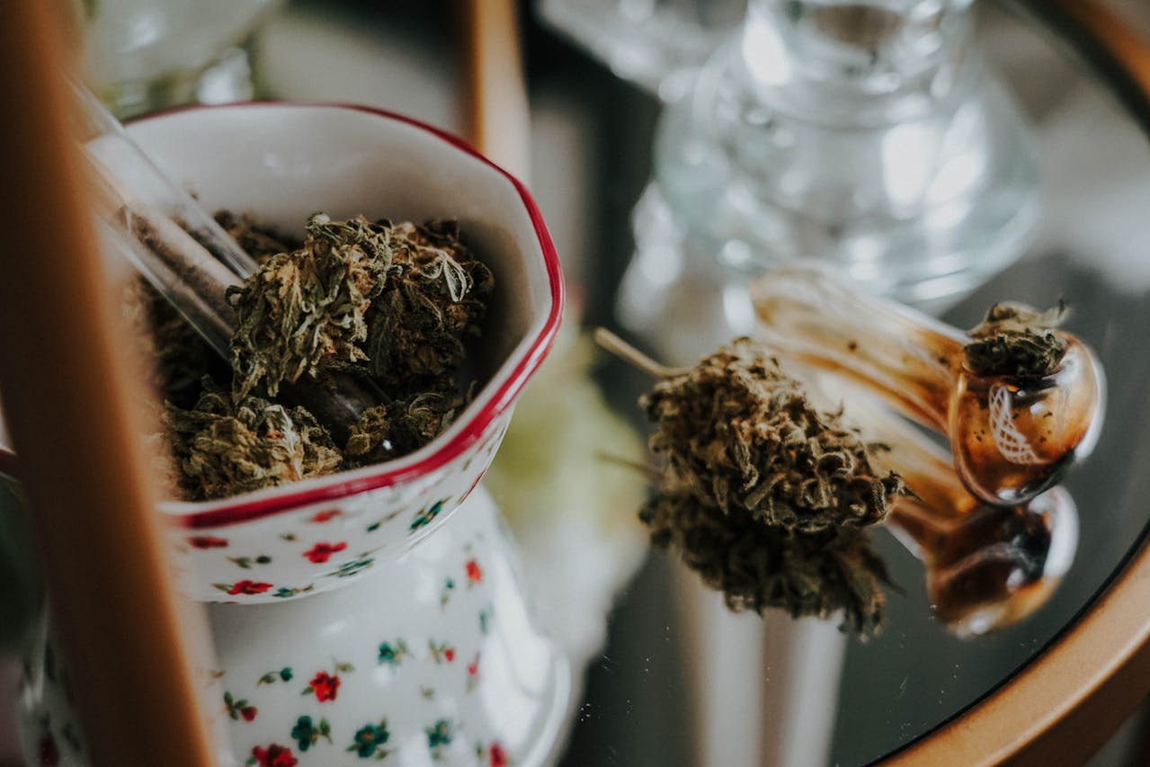 White and red bowl containing thc flower and thc flower to the right of the bowl, on a reflective surface. 